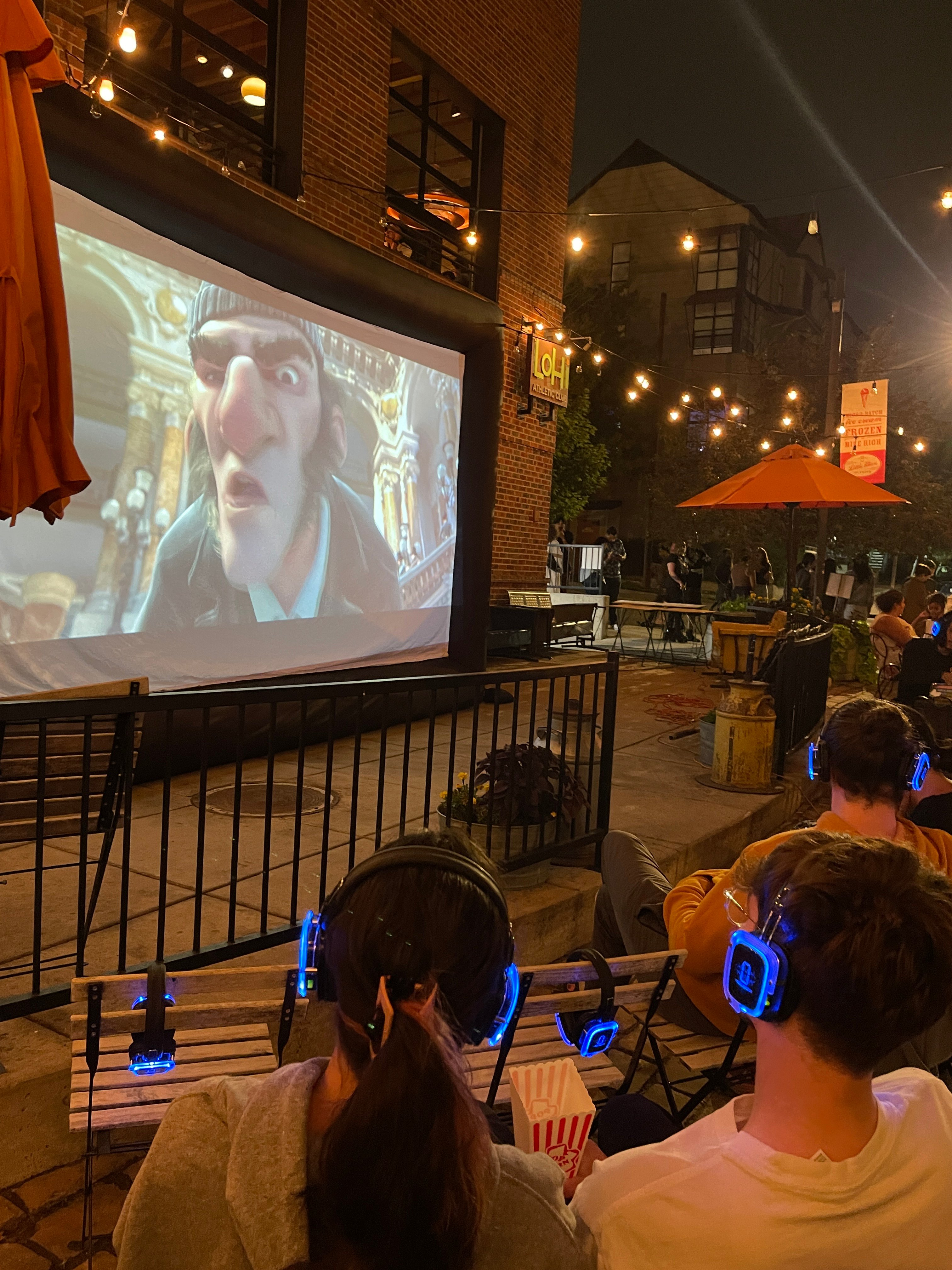 outdoor plaza at night, guests in headphones watching a projected movie.